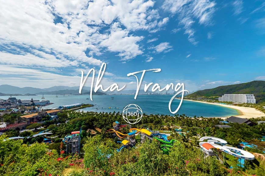 Aerial view of Nha Trang coast with a sandy beach, turquoise water, and a colorful water park in the foreground amid green hills.